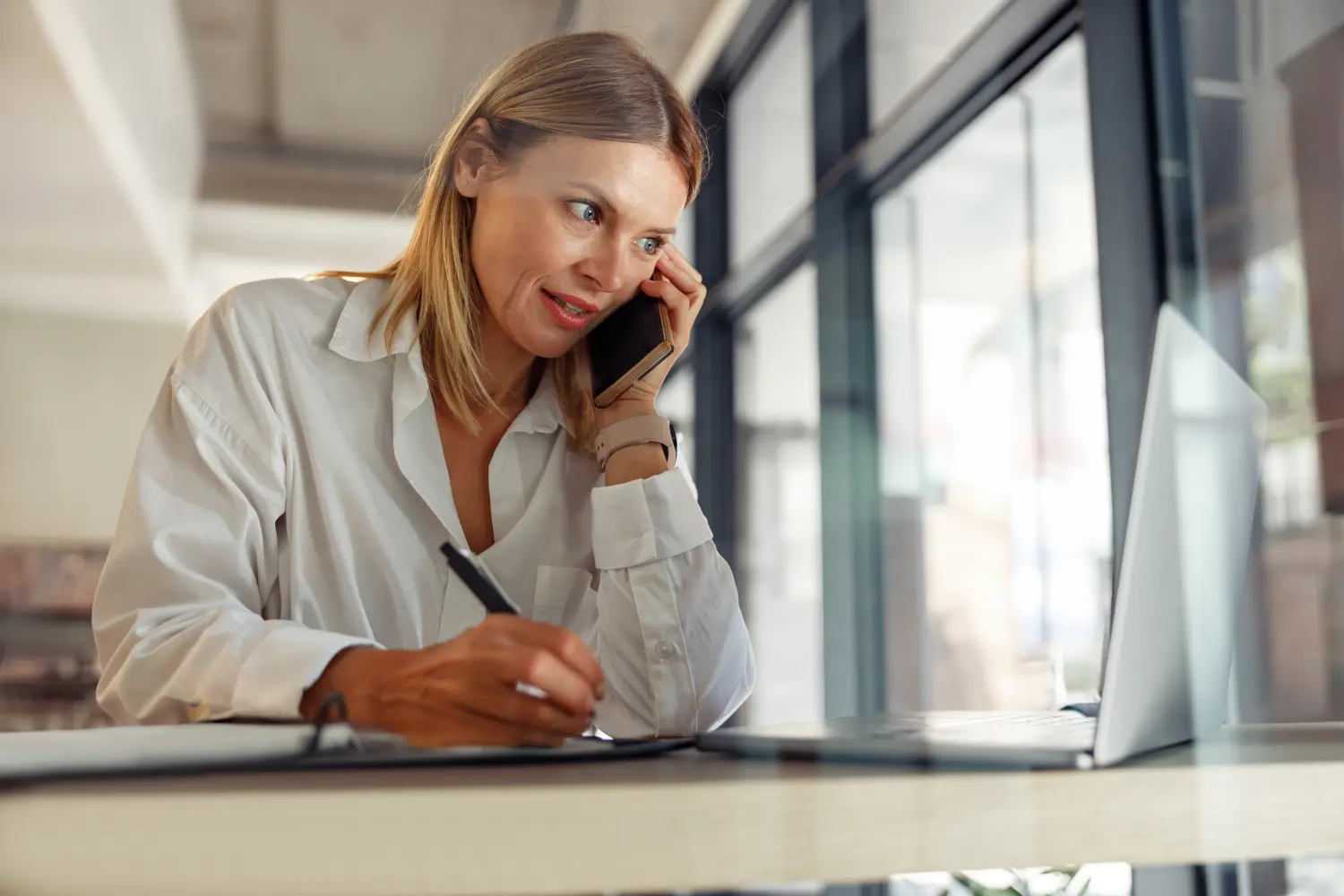 Unternehmerin macht sich Notizen und telefoniert mit dem Kunden, während sie im Coworking sitzt